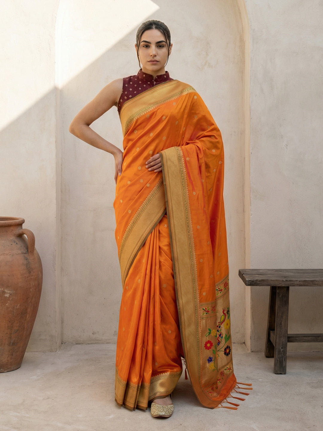 Woman wearing an orange saree with a gold border indoors.