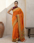 Woman wearing an orange saree with a gold border indoors.