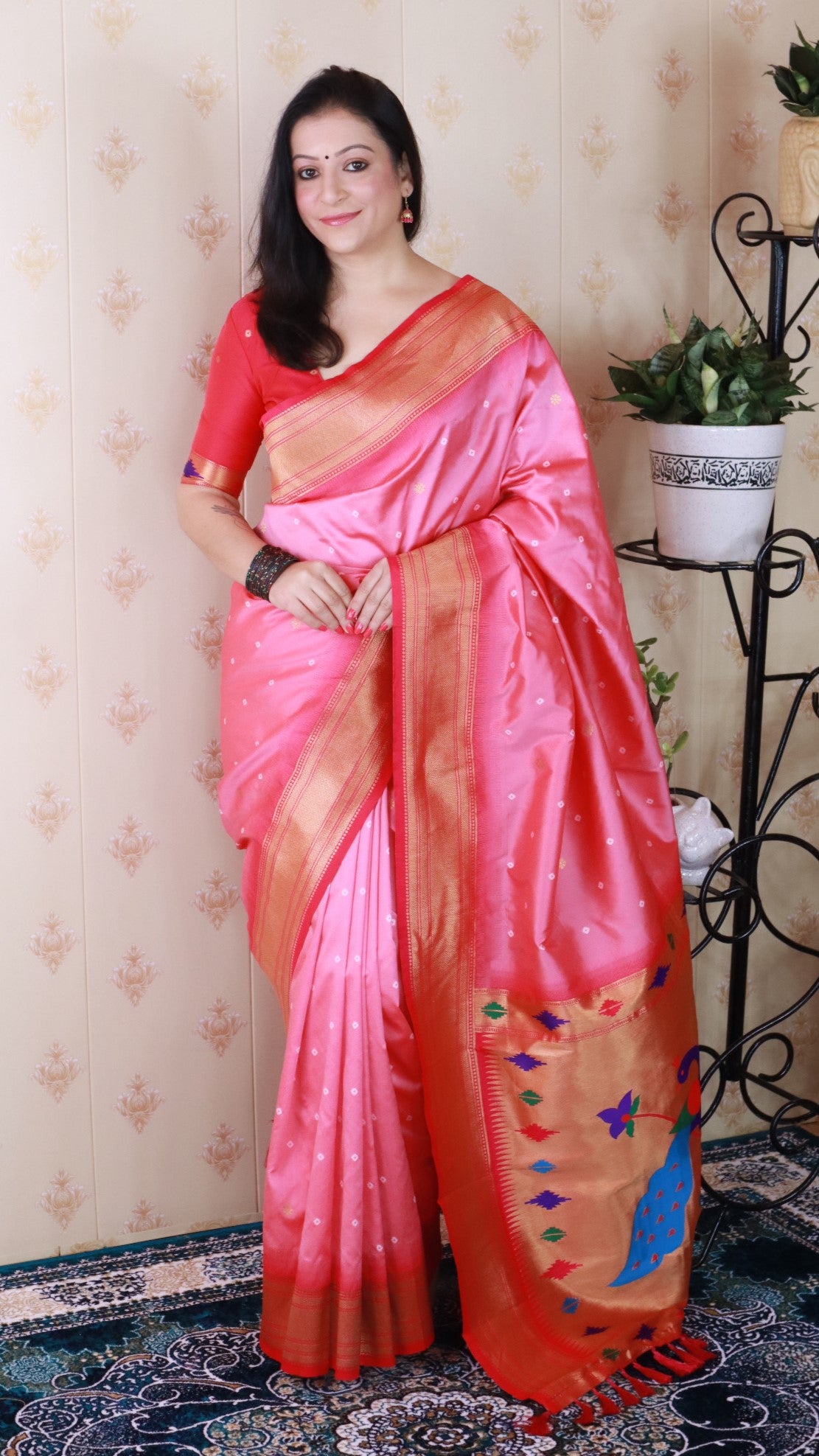 Woman wearing a pink and orange saree with a decorative border indoors.
