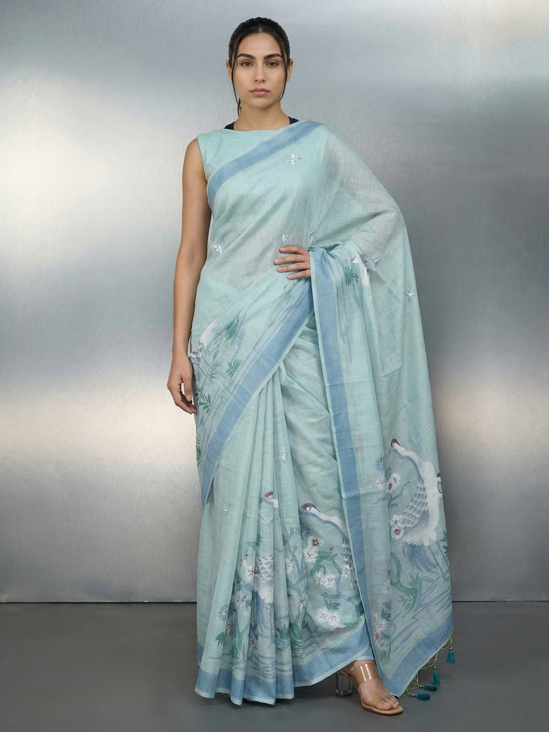 Woman wearing a light blue saree with a subtle pattern on a gray background