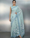 Woman wearing a light blue saree with a subtle pattern on a gray background