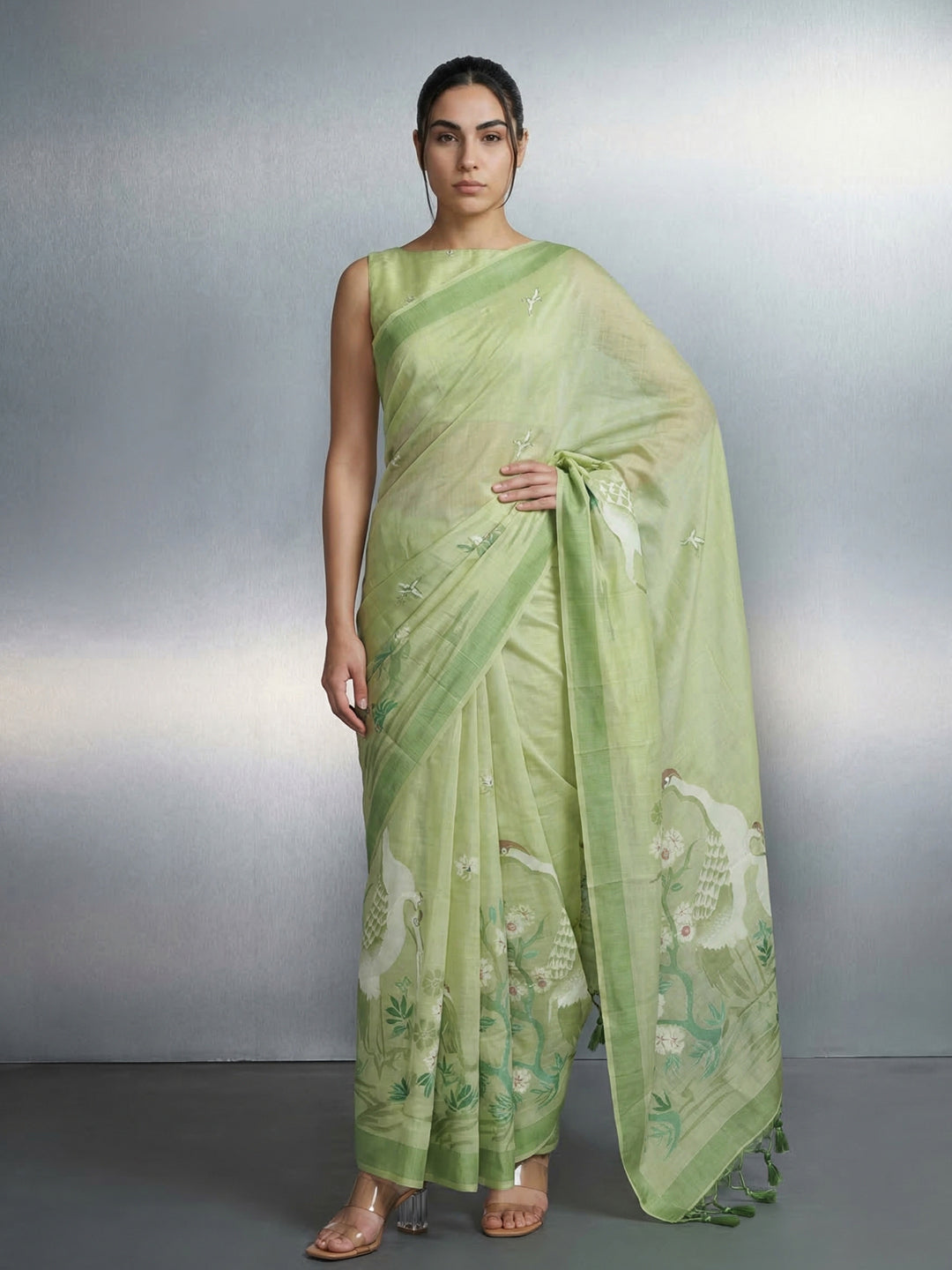 Woman wearing a light green saree with a subtle pattern on a plain background