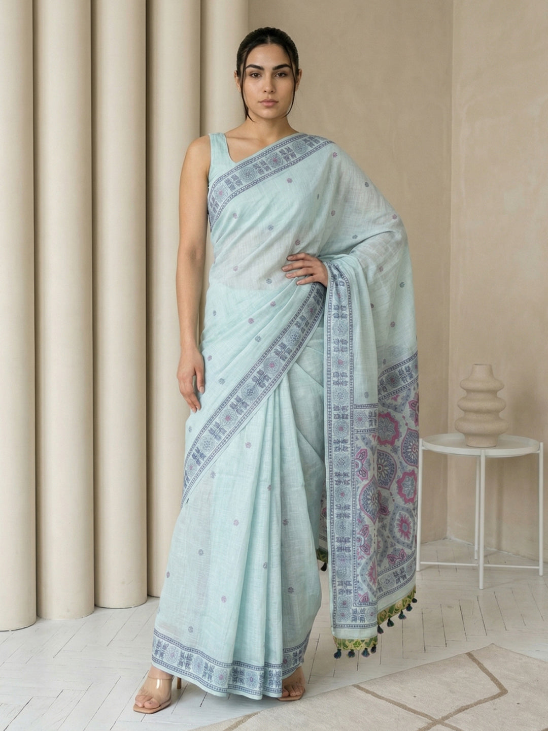 Woman wearing a light blue saree with a patterned border in a minimalistic setting.