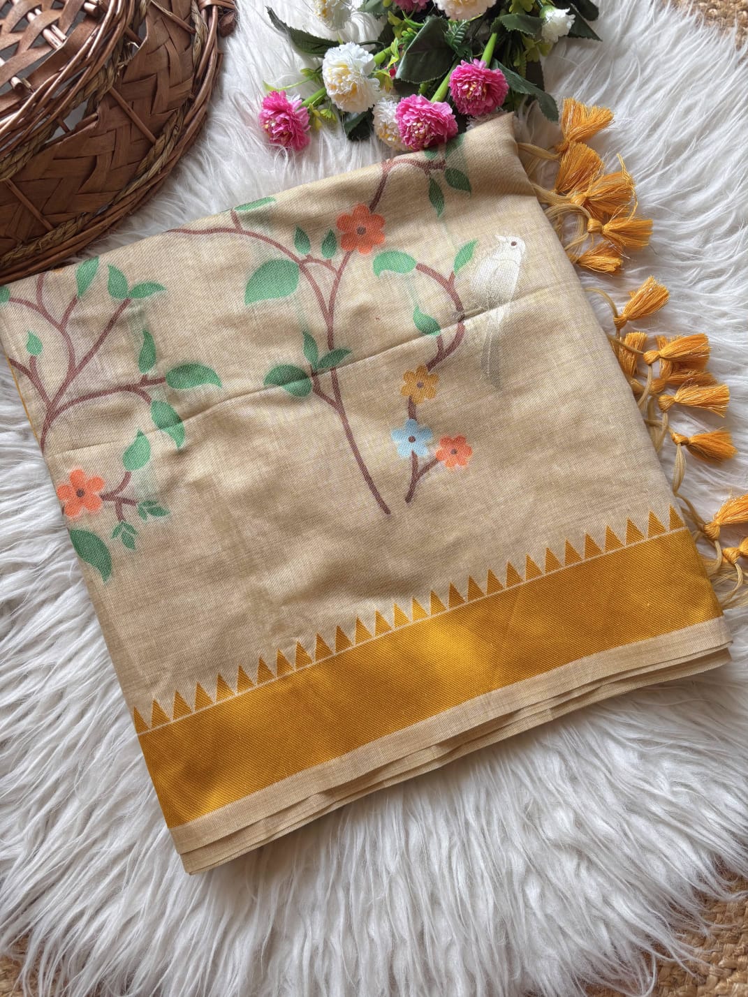 Beige fabric with floral embroidery and yellow border on a fluffy white surface.