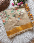 Beige fabric with floral embroidery and yellow border on a fluffy white surface.
