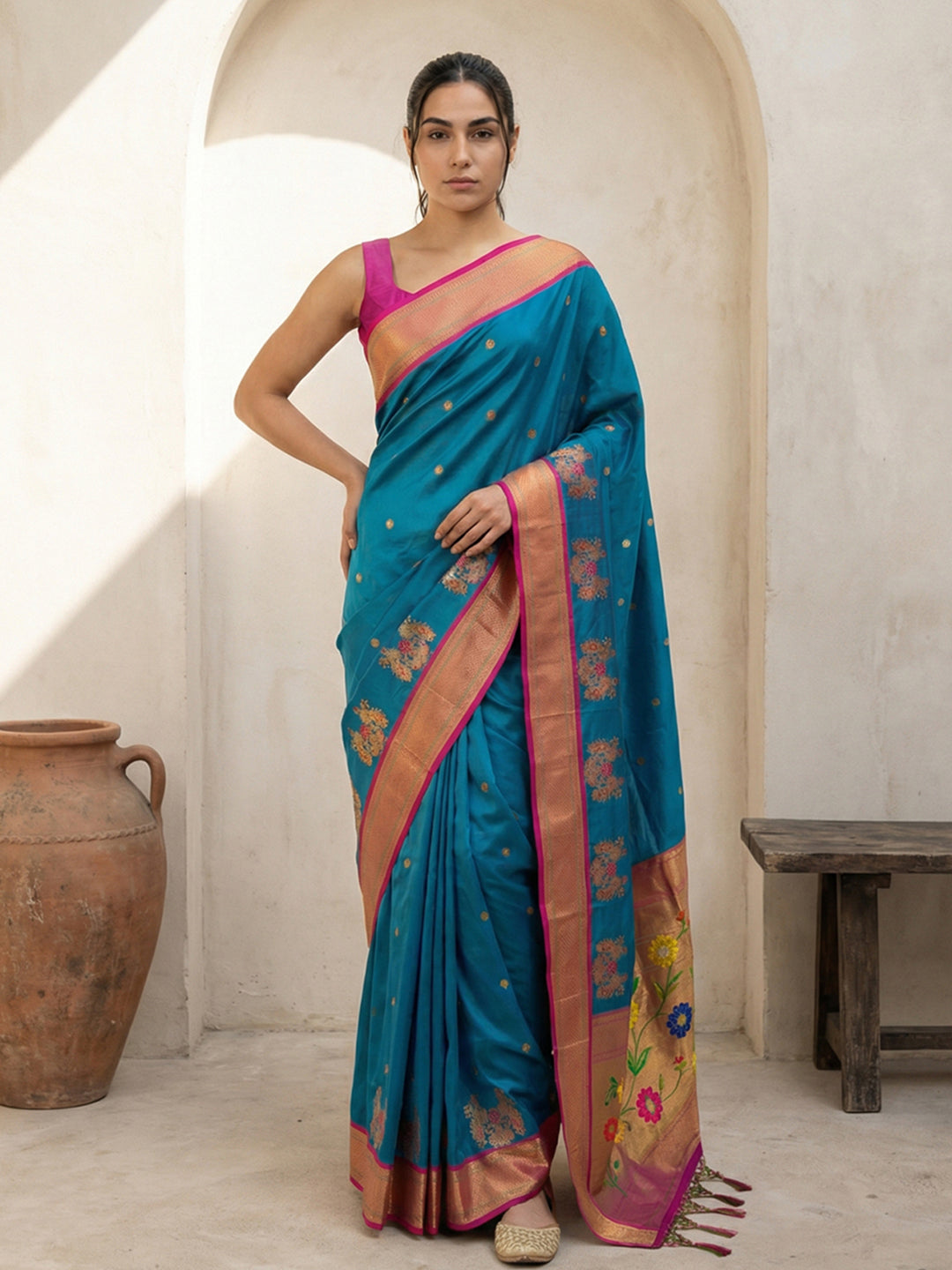 Woman wearing a blue saree with a pink border in an indoor setting.