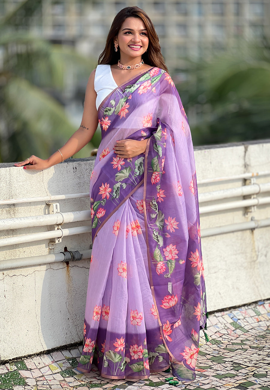 Woman wearing a purple saree with floral patterns standing outdoors.