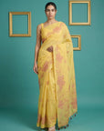 Woman wearing a yellow saree with floral patterns against a teal background