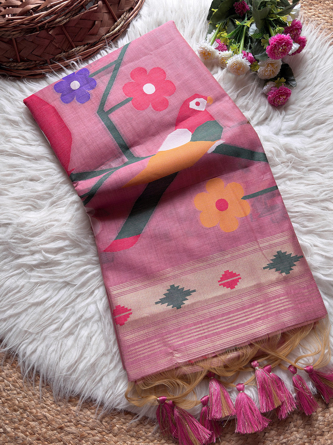 Pink scarf with floral and bird design on a white surface with flowers and a basket.