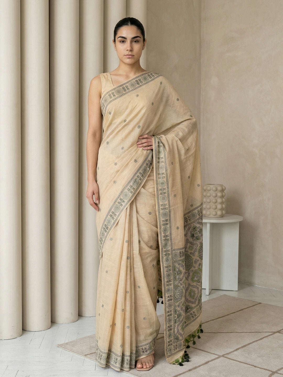 Woman wearing a beige saree with intricate patterns in a minimalistic setting.