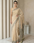Woman wearing a beige saree with intricate patterns in a minimalistic setting.