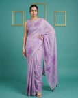 Woman wearing a purple saree with a floral pattern on a teal background