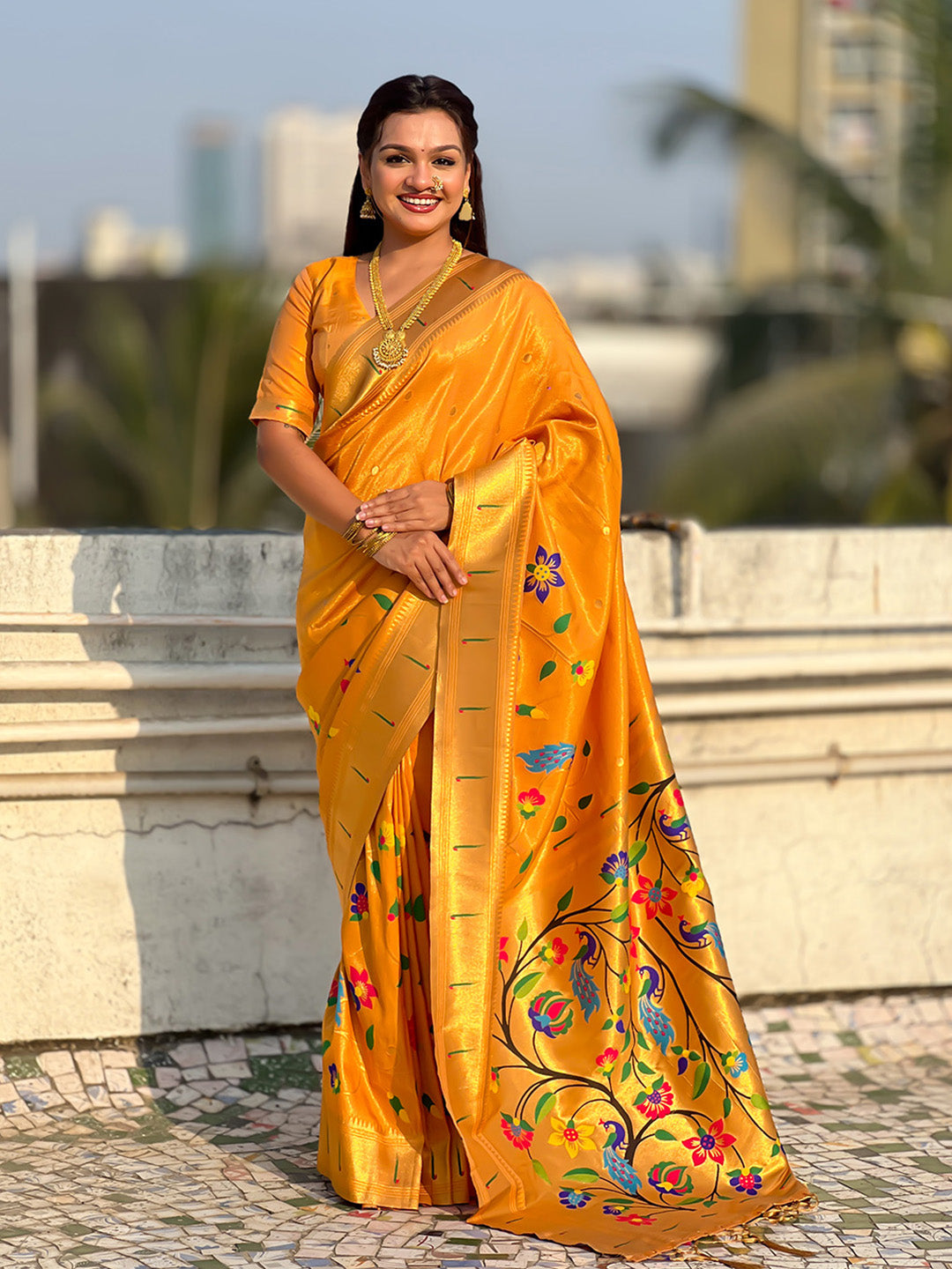 Woman in a bright yellow saree with floral patterns standing outdoors.