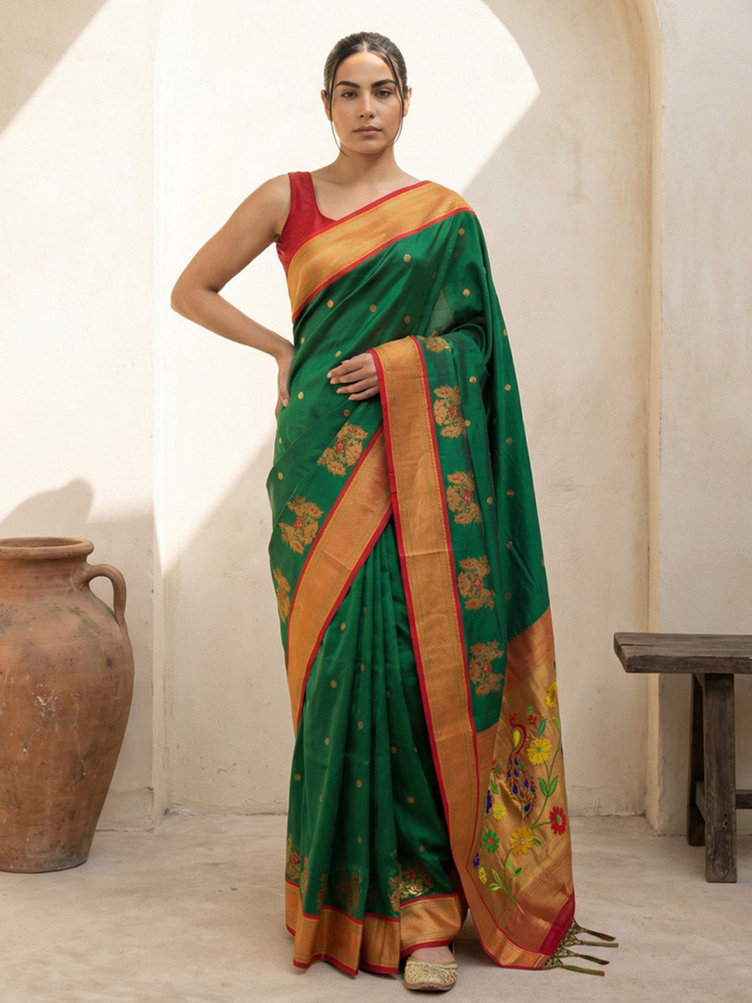 Woman wearing a green and orange saree in a room with a white wall and wooden bench.