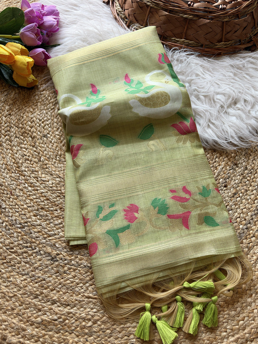 Light green scarf with floral patterns on a textured surface with flowers and a basket in the background.